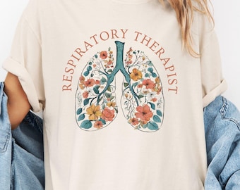 May include: Cream-colored t-shirt featuring a floral lung design. The lungs are filled with orange, yellow, and pink flowers, with a teal-colored trachea. The words "Respiratory Therapist" are arched around the lung design.