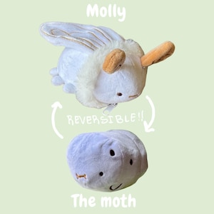 May include: A reversible moth plush toy, named "Molly" at the top. The moth is white with tan accents and a fluffy collar. The reverse side is a grey, rounded shape with a stitched smile and eyes. Text reads "REVERSIBLE!!" and "The moth."