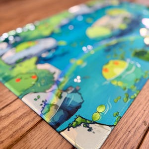 Puede incluir: Una alfombrilla de rat&oacute;n rectangular con una vibrante y colorida ilustraci&oacute;n de una escena acu&aacute;tica caprichosa. El dise&ntilde;o incluye tonos de azul, verde y amarillo, con representaciones detalladas de agua, plantas y criaturas de dibujos animados. Los bordes est&aacute;n cuidadosamente cosidos.