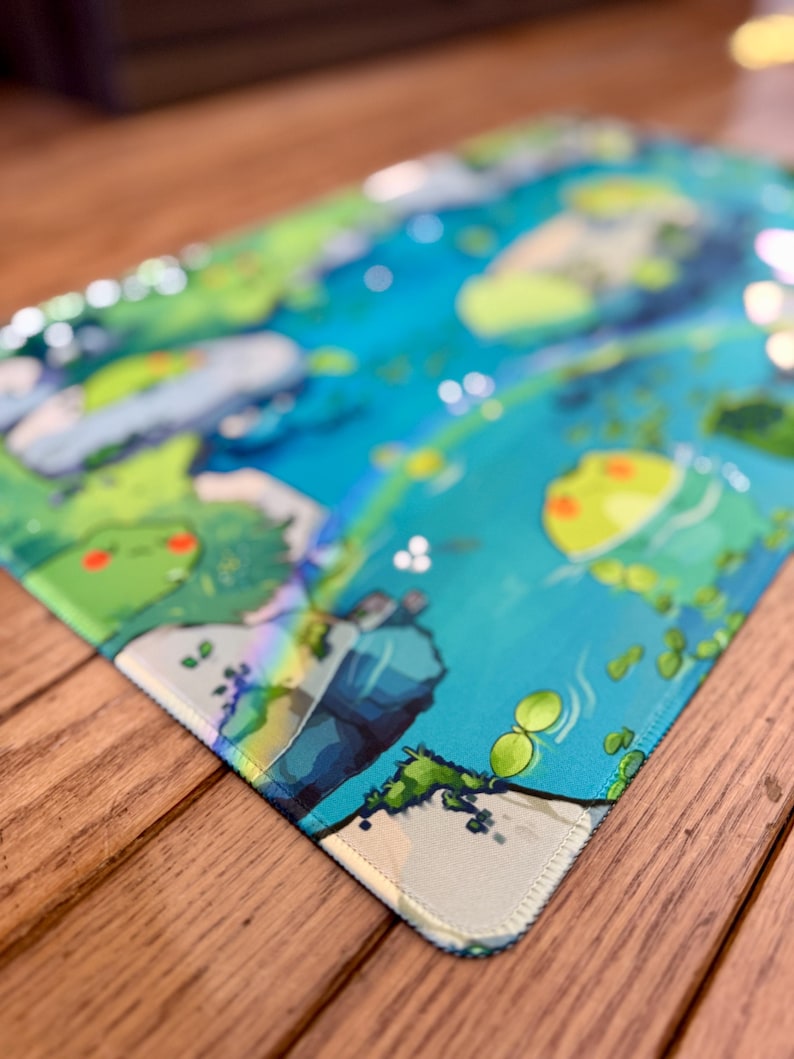 Puede incluir: Una alfombrilla de rat&oacute;n rectangular con una vibrante y colorida ilustraci&oacute;n de una escena acu&aacute;tica caprichosa. El dise&ntilde;o incluye tonos de azul, verde y amarillo, con representaciones detalladas de agua, plantas y criaturas de dibujos animados. Los bordes est&aacute;n cuidadosamente cosidos.