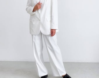 May include: A white blazer with a single button closure and a white pair of wide-leg pants. The person is wearing black loafers.
