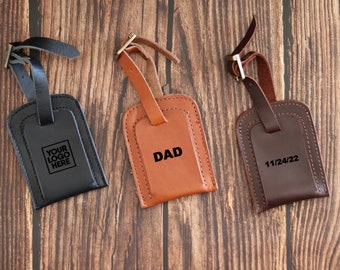May include: Three leather luggage tags with different text. The first tag is black with the text "YOUR LOGO HERE". The second tag is brown with the text "DAD". The third tag is dark brown with the text "11/24/22".