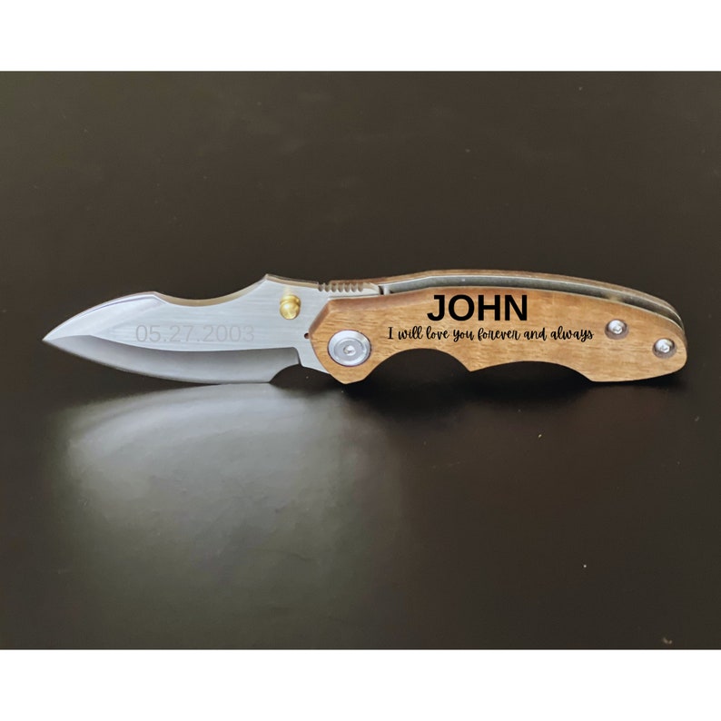 May include: A brown wooden pocket knife with a silver blade. The knife has the name "JOHN" and the text "I will love you forever and always" engraved on the handle. The date "05.27.2003" is engraved on the blade.