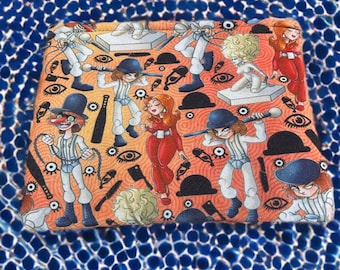 Può includere: Un tessuto rettangolare con un motivo ripetuto di personaggi in abiti bianchi e neri, bombette e armi. Il design include occhi, bombette nere e altri elementi grafici. Lo sfondo è una superficie blu strutturata.