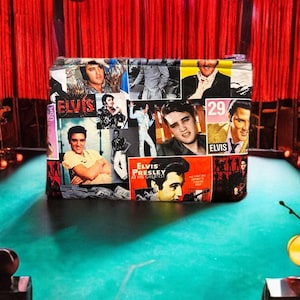 May include: A black zippered pouch featuring a collage of images of Elvis Presley. The images include Elvis in various poses and outfits, as well as album covers and concert posters. The text "Elvis Presley at His Greatest" is visible on one of the album covers.