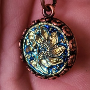 Può includere: Una collana con catena in rame con un ciondolo rotondo che presenta un cammeo in vetro iridescente blu e oro con un motivo floreale.