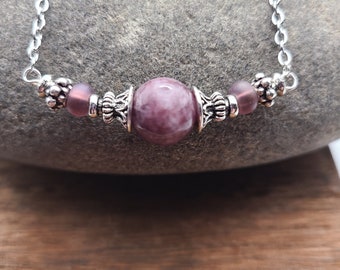 May include: A silver chain necklace with a pink and white agate bead and two smaller pink glass beads. The necklace is on a gray rock surface.