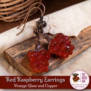 May include: A pair of red raspberry earrings made of vintage glass and copper. The earrings feature a cluster of red glass beads, resembling raspberries, suspended from copper ear wires. The text "Red Raspberry Earrings Vintage Glass and Copper" is visible.