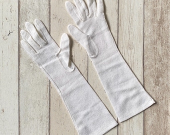 May include: A pair of long white gloves made of a soft, stretchy fabric. The gloves are seamless and have a smooth finish.