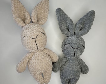May include: Two crocheted bunny toys. One is beige and the other is gray. Both have black eyes and a stitched nose.