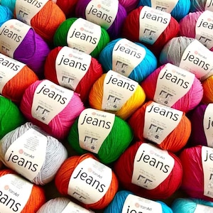May include: A collection of yarn balls in various colours, including red, orange, yellow, green, blue, purple, and grey. Each ball has a label that reads "YarnArt jeans".