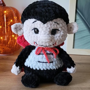 Puede incluir: Muñeco de vampiro de peluche hecho a mano, con cabeza y cuerpo negros, cara gris claro, pajarita y capa rojas. El muñeco tiene ojos negros grandes y pequeños colmillos, perfecto para Halloween o como juguete infantil.