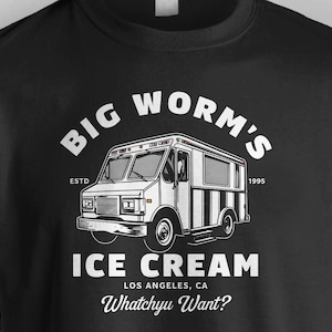 May include: Black t-shirt with a white graphic of an ice cream truck with the text "Big Worm's Ice Cream" and "Whatchyu Want?"  The truck has a white and black striped design. The text "Estd 1995" is also included.