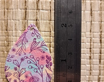 Op de afbeelding: Een traanvormige leren oorbel met een bloemenpatroon in tinten roze, paars en blauw. De oorbel is ongeveer 5 cm lang.