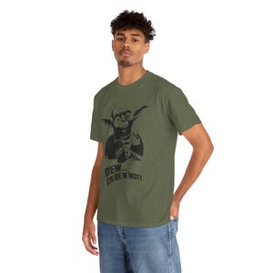 May include: Olive green t-shirt featuring a black graphic of a cartoon character holding a beverage. The text "DEW... OR DEW NOT!" is printed below the graphic. The shirt is made of a soft material.