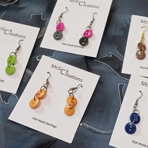 May include: Five pairs of fish hook earrings with different colored buttons. The earrings are displayed on white cards with the text "McSiC Creations" and "Fish Hook Earrings".