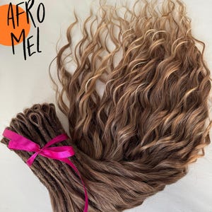 Puede incluir: Extensiones de cabello rizado marrón y rubio con una cinta rosa brillante. El texto "AFRO MEL" está en letras negras sobre un círculo naranja.