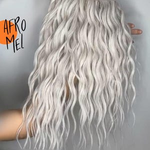 May include: Wavy, light gray hair extensions. The hair has a natural, textured appearance with a slight wave pattern. The text "AFRO MEL" is written in black script with an orange circle behind the text.