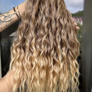 May include: Wavy, light brown and blonde hair extensions. The hair has a natural, sun-kissed ombre effect, transitioning from darker roots to lighter tips. The text "Photo in natural street lighting" is visible.