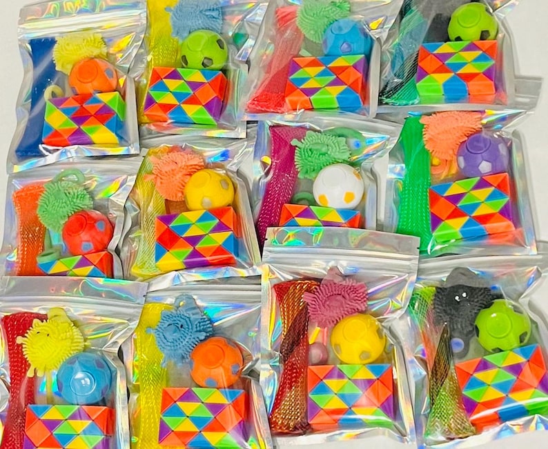 May include: A collection of clear, sealed bags filled with colorful fidget toys. Each bag contains a variety of items, including textured balls, geometric puzzles, and stretchy tubes. The toys are in various bright colors, including red, yellow, blue, and green.
