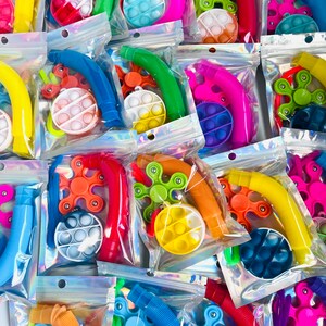 K&ouml;nnte beinhalten: Sortiment an bunten Fidget-Spielzeugen, verpackt in durchsichtigen Plastikt&uuml;ten. Jede T&uuml;te enth&auml;lt ein Pop-it, einen Fidget Spinner und einen biegsamen Strohhalm. Die Spielzeuge sind in verschiedenen Farben, darunter Blau, Gr&uuml;n, Gelb, Orange, Pink und Lila.