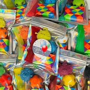 May include: A collection of clear plastic bags filled with colorful toys. Each bag contains a variety of items, including spiky balls, rainbow-colored puzzles, and other small toys. Some bags have a sticker that says "Thank you for celebrating with me! -Tristen."