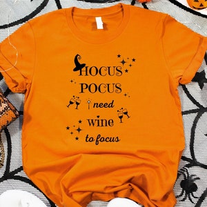 Peut inclure: T-shirt orange avec un texte noir qui dit "Hocus Pocus I need wine to focus" avec un chapeau de sorcière et des étoiles.