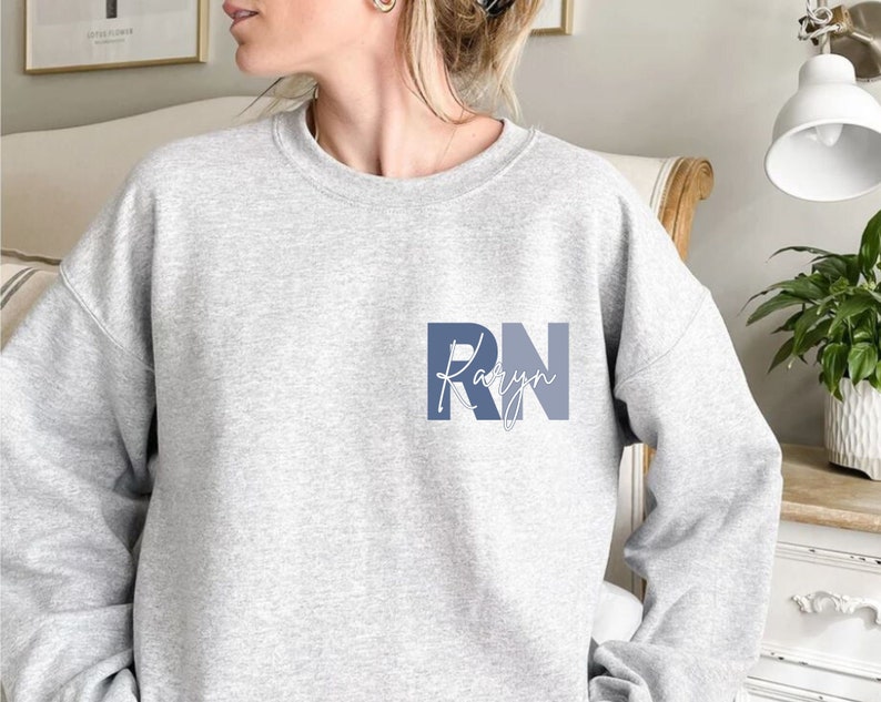 Puede incluir: Sudadera gris con un gr&aacute;fico azul y blanco que dice "RN Karyn".