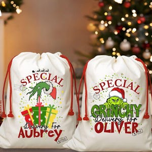 May include: Two white drawstring gift bags with red drawstrings. One bag features a Grinch design with the text "Special Delivery for Aubrey." The other bag has a Grinch design with the text "Special Grinchy Delivery for Oliver."