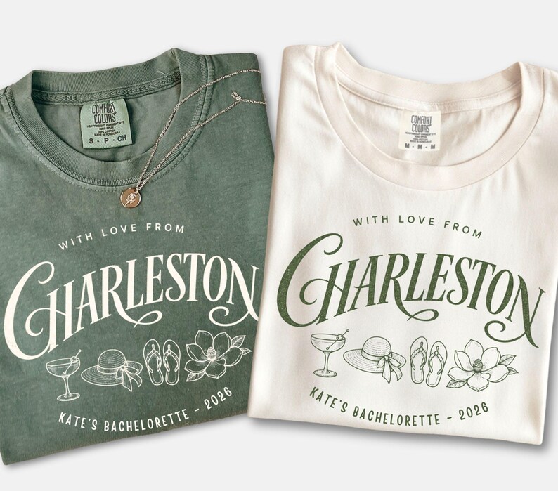 May include: A sage green t-shirt and a white t-shirt, both featuring the text 'WITH LOVE FROM CHARLESTON' and 'KATE'S BACHELORETTE - 2026' in a script font, accompanied by line art illustrations of a cocktail, a sun hat, flip-flops, and a magnolia.