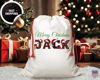 May include: A white drawstring Christmas gift bag with the text "Merry Christmas Jack". The name "Jack" is in a red and black plaid pattern with Santa hats. Red drawstring closure.