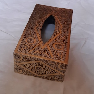 May include: A gold-colored metal tissue box cover with an intricate embossed design. The cover has a rectangular shape with a slot for tissues.