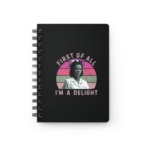 May include: Black spiral notebook with a retro-style graphic of a woman in a nurse's uniform. The graphic has a pink, green, and white colour scheme and the text "First of all, I'm a delight".