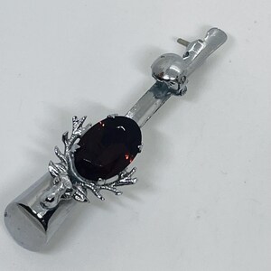 May include: A silver bottle stopper with a deer head design and a large, oval, dark red gemstone. The stopper also features a skull and antler-like accents, creating a unique and decorative piece.