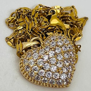 May include: A gold heart-shaped pendant necklace with a chain. The pendant is covered in small, clear cubic zirconia stones.