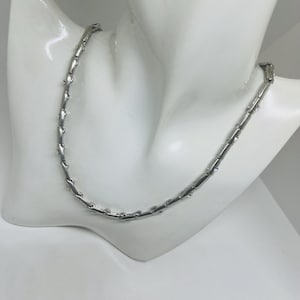 May include: A silver necklace with a distinctive design, shown on a white mannequin bust. The necklace comprises rectangular links joined by smaller, decorative features. The jewellery is displayed against a plain white background.