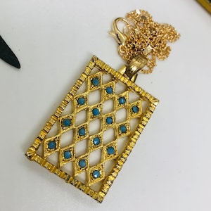 May include: A gold-tone pendant necklace with a rectangular frame design. The frame is decorated with a diamond pattern and blue gemstones.