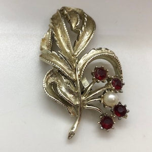 May include: A silver tone brooch with a leaf design and red and white stones.