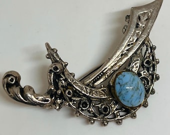 Può includere: Un fermaglio d'argento con una pietra blu incastonata in un design a filigrana.
