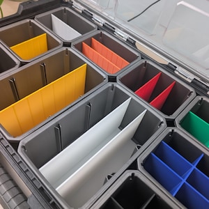 Può includere: Una valigetta organizer in plastica nera con coperchio trasparente, dotata di scomparti grigi. L'interno è organizzato con divisori rimovibili in giallo brillante, bianco, arancione, rosso, verde e blu per creare diverse sezioni di spazio.