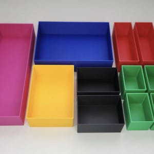 May include: A collection of colorful storage bins in various sizes. The bins are in shades of pink, blue, yellow, red, black, and green. The arrangement includes rectangular and square shapes, suitable for organizing items.