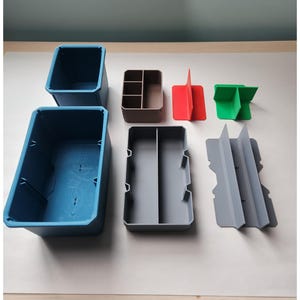 May include: A collection of modular storage components including two blue rectangular bins, a brown multi-compartment tray, a grey divided tray, a red T-shaped divider, a green cross-shaped divider, and a grey dual-slotted divider piece.