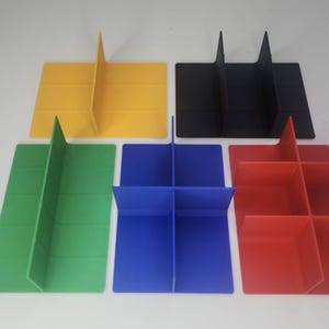 Puede incluir: Cinco divisores de cartón de colores en amarillo, negro, verde, azul y rojo. Los divisores son rectangulares con ranuras verticales y horizontales para crear compartimentos. Los divisores están dispuestos sobre una superficie blanca.