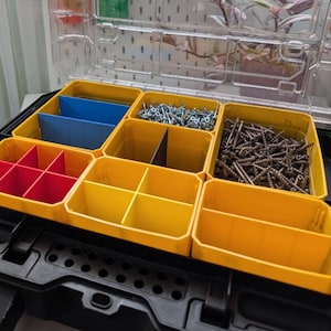 Może przedstawiać: Czarna i przezroczysta plastikowa skrzynka narzędziowa z żółtymi, czerwonymi i niebieskimi przegródkami. Przegródki zawierają różne śruby i elementy mocujące. Skrzynka narzędziowa jest otwarta, ukazując zawartość i organizację.