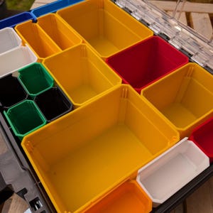 May include: A multi-colored organizer with various sized plastic bins. The bins are yellow, red, white, green, black, and blue. The organizer is designed to hold small items and tools.