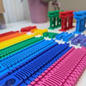May include: A set of colorful plastic train tracks in red, orange, yellow, green, blue, and pink. The tracks are arranged in a rainbow pattern and are designed for use with toy trains.