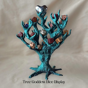 May include: A teal green tree-shaped dice holder with a silver heart at the top. The tree has many branches that hold various coloured dice. The text "Tree Goddess Dice Display" is at the bottom of the image.