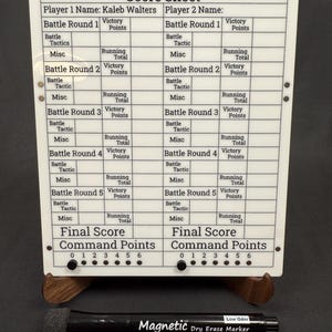 May include: A white dry-erase score sheet with a wooden stand, featuring sections for battle rounds, victory points, and command points. Includes a black magnetic dry-erase marker. The text "Score Sheet" is at the top.