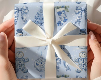 Puede incluir: Un regalo envuelto con papel de regalo azul claro con un patrón repetido de adornos navideños azules y blancos, muñecos de nieve y hombres de jengibre. Una cinta color crema está atada alrededor del regalo.