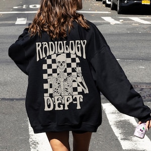Op de afbeelding: Zwart sweatshirt met een witte afbeelding van een skelet met de tekst "RADIOLOGY DEPT" in een geruit patroon.